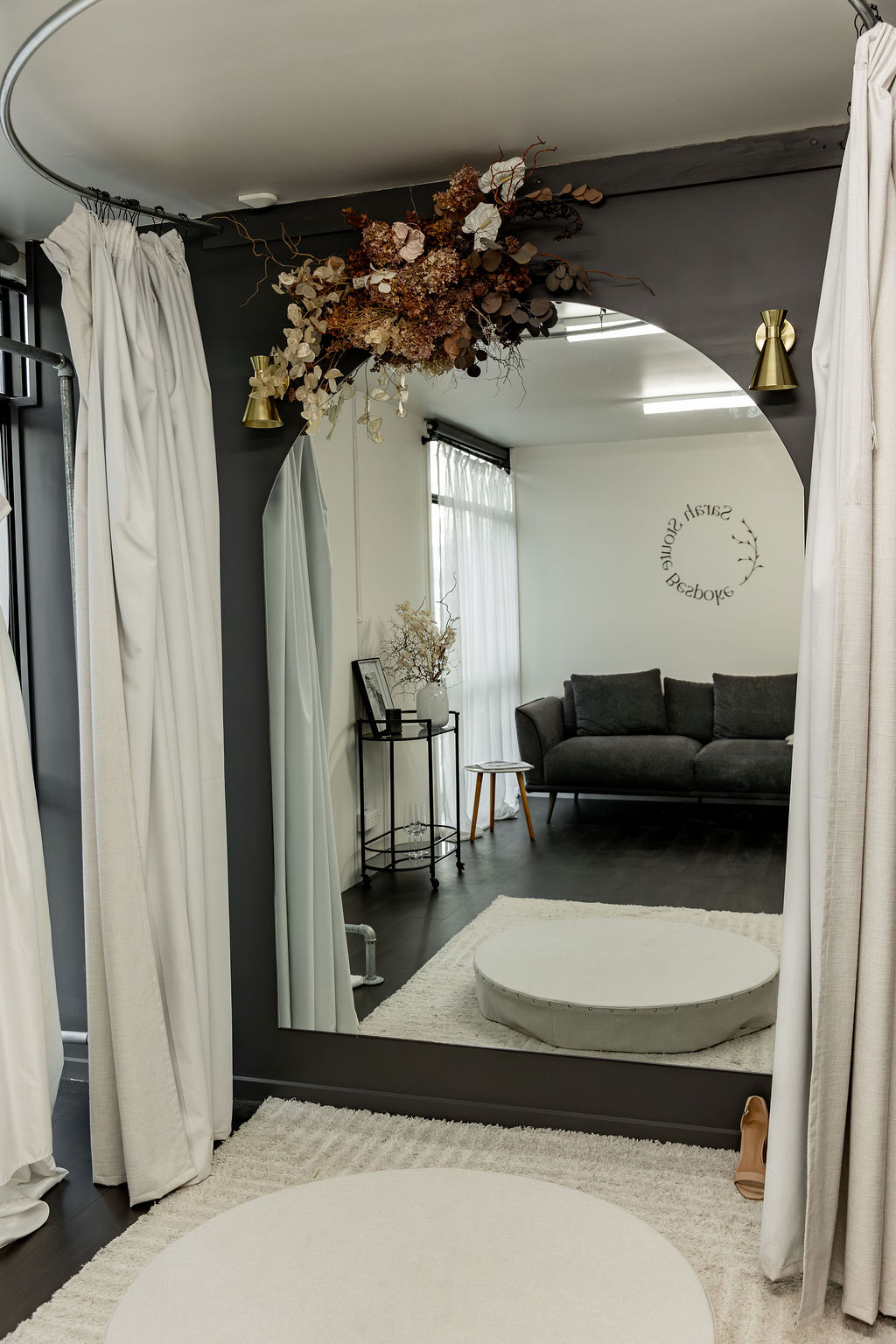 A curtained fitting room in the Christchurch studio, with an arched mirror and dried florals